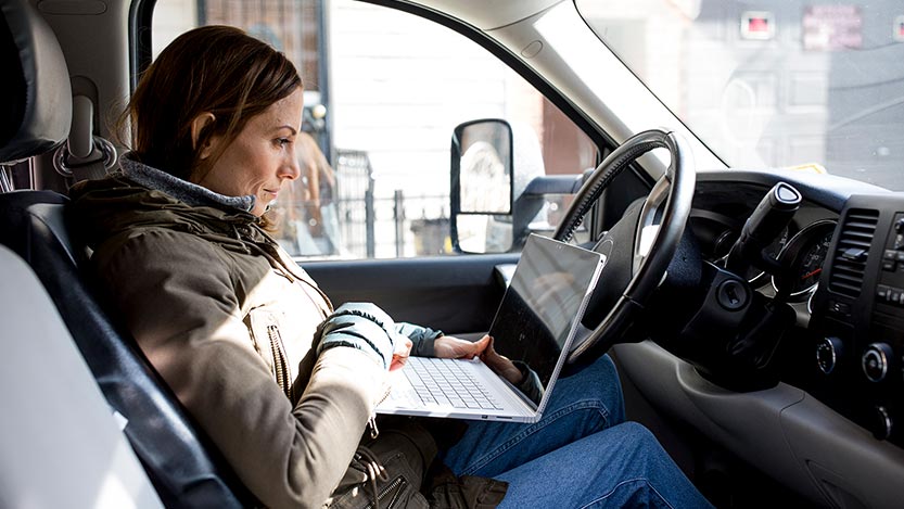 A Digital Nomad works on their laptop in the driver seat of an SUV.