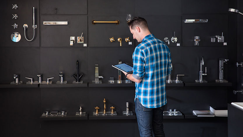 In front of a display wall for sink faucets, a man checks inventory on a Microsoft Surface tablet PC.