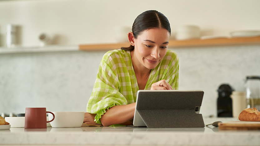 A woman sitting in a kitchen working on a tablet.