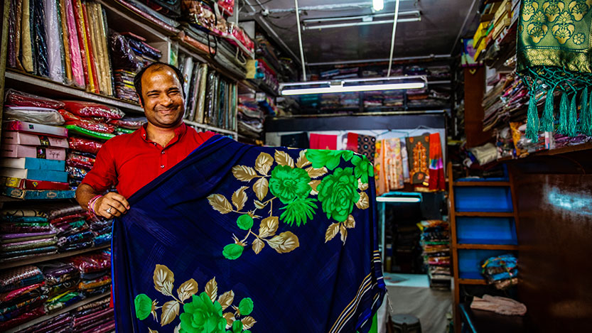 A man in a market shows fabrics from his store.