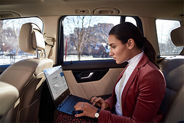 A woman sitting in the back of a car works on her laptop computer