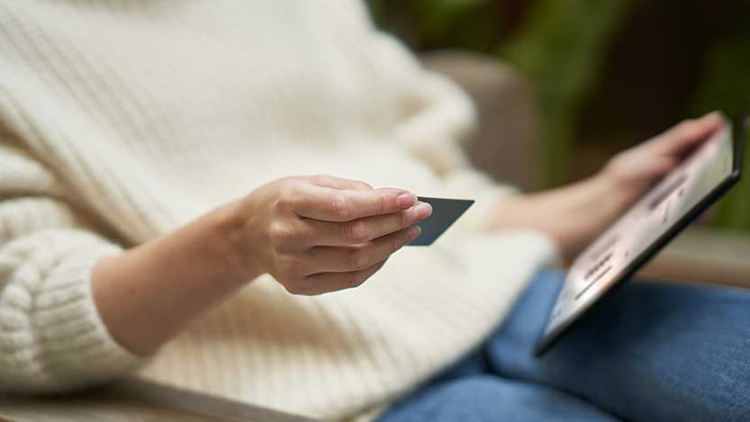 A person sitting down holds a card in one hand and a tablet in the other.