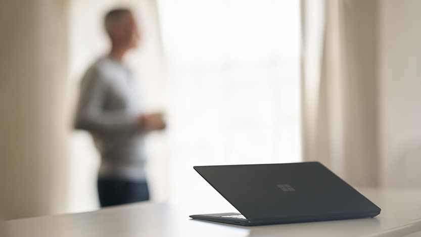 A Microsoft laptop on a desk with a blurred person in the background.