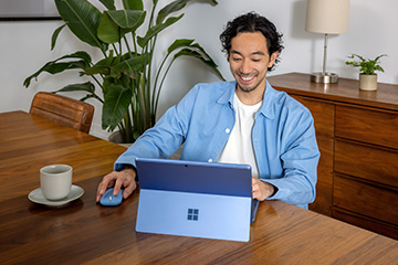 A man sitting at a table smiles while working on his laptop computer.
