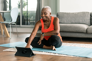 Woman sitting on a yoga mat interacting with a tablet.