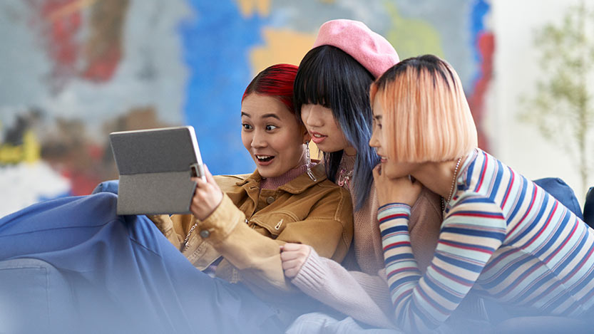 Three young women watching videos together on a tablet.