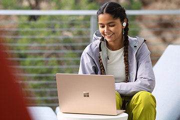 A young woman sitting outside smiles while working on her computer.