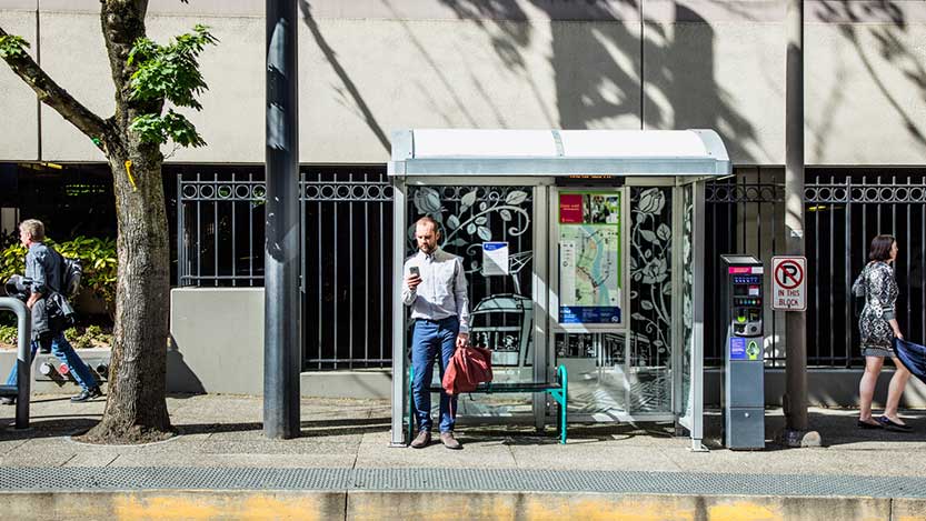 A man waiting at a bus stop checks his phone.