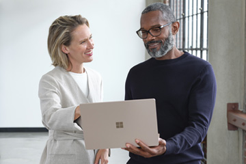 Two people smile as they hold a laptop in front of them.