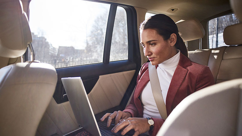 Person typing on a laptop while sitting in a car.