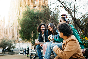 Four people smiling while having coffee in a park.