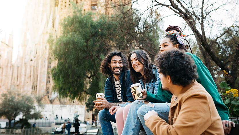 Four people smiling while having coffee in a park.