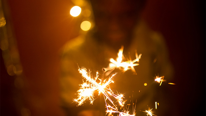 Person smiling while holding a festive sparkler.