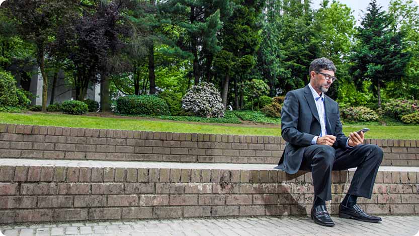 Businessperson looking at their mobile phone while sitting in a park bench.
