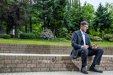 Businessperson looking at their mobile phone while sitting in a park bench.