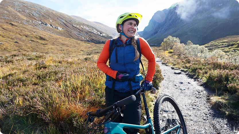 Cyclist holding a bike on the mountain while smiling.