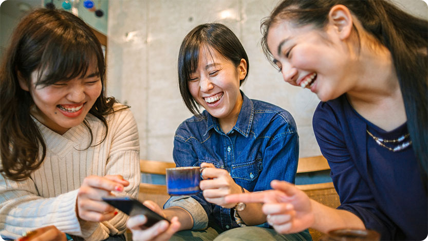 Three female coworkers laughing while looking at a smartphone.
