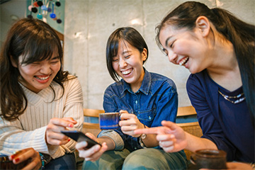 Three female coworkers laughing while looking at a smartphone.