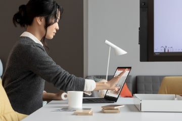Junge-Frau-mit-schwarzen-Haaren-die-ein-graues-Wollhemd-trägt-an-ihrem-Schreibtisch-sitzt-und-an-ihrem-Laptop-arbeitet.