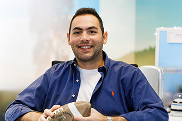 Male office worker in modern workplace, seated at cubicle desk while holding football, smiling and looking directly at camera.