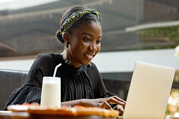 A young woman smiles while looking at a laptop.