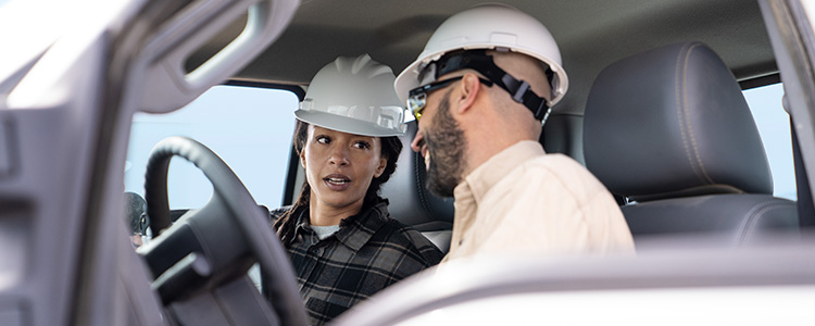 A man and a woman wearing safety helmets converse inside a truck.