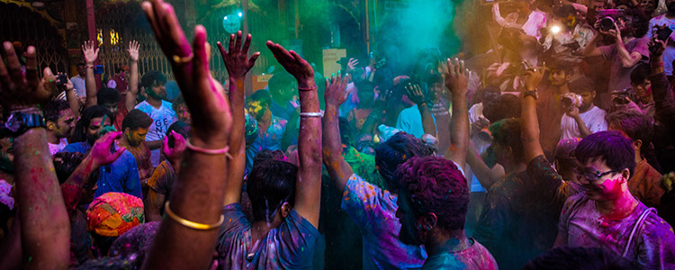 A group of young people raise their hands and celebrate covered in paint while participating in a color festival.