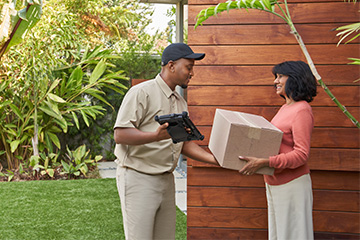A delivery man hands a box to a woman outside her door.