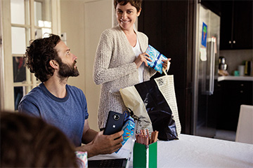 A woman holds a gift and a bag while a man looks at her expectantly.
