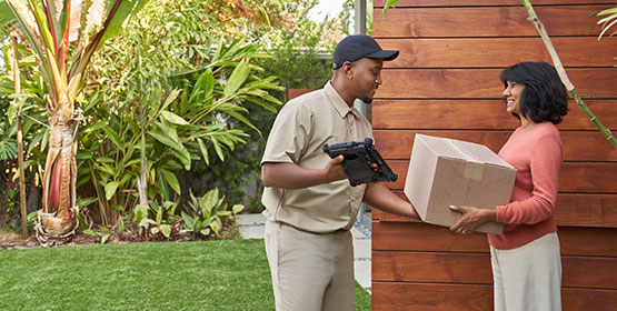 A delivery man hands a box to a woman outside her door.