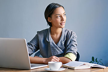 A woman looks thoughtfully into the distance as she works on her laptop PC.