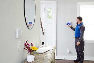 An ADT worker interacts with a tablet attached to the wall of a house.