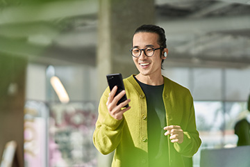 A man with a green sweater smiles while holding up his phone.