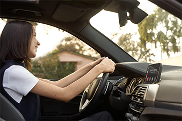 A woman smiles and looks ahead while she's driving a car.