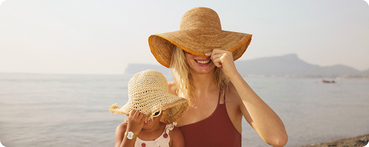 Happy mother and child wearing hats at the beach.