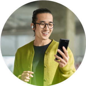 Person smiling while wearing wireless earbuds and holding a mobile phone.