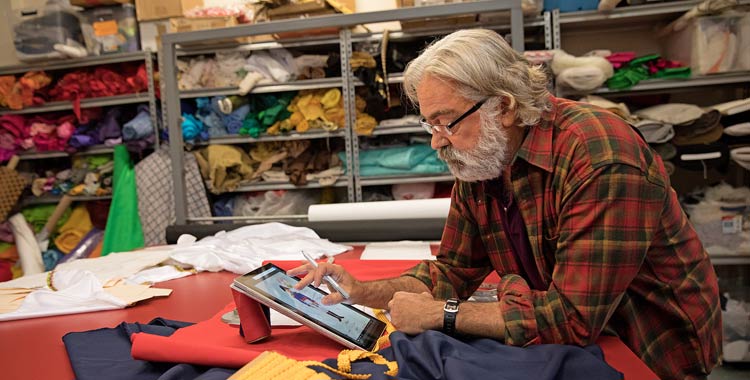 In a grocery store, an older man with a beard and long grey hair works on a tablet PC.