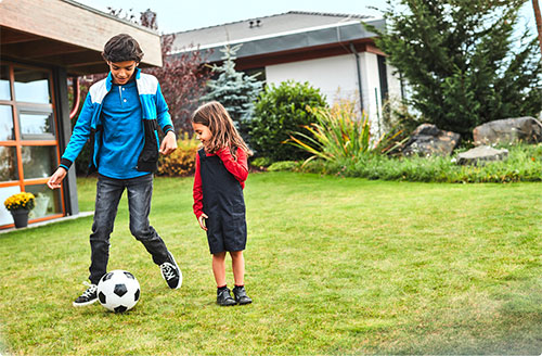 Two children play with a soccer ball in a yard.