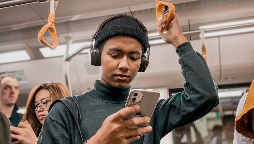 Person with headphones using a smartphone in public transport.