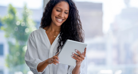 A woman smiles while holding a tablet.