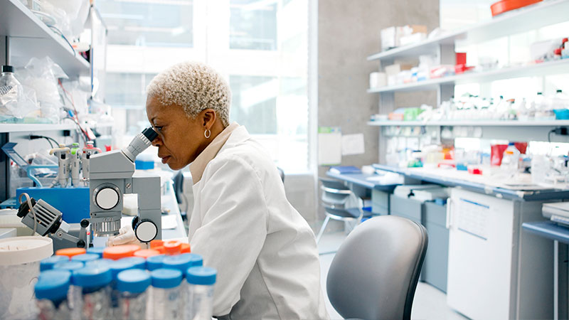 A scientist in a pharmaceutical lab looks through her microscope.