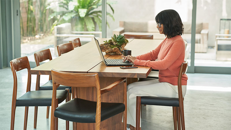 A woman sitting at a table works on her laptop computer.