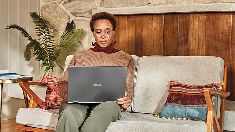 A woman sitting on a couch works on her laptop computer.